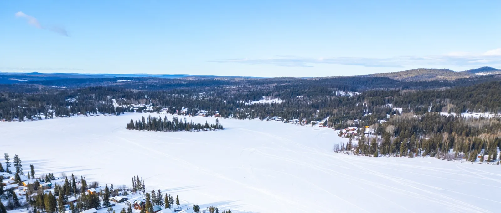 Snow-covered homes and forest beside the frozen surface of Deka Lake