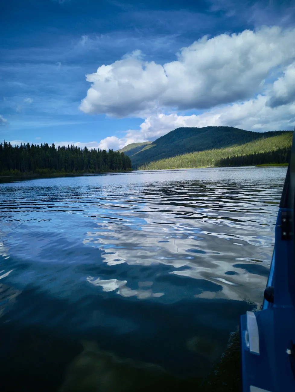Deka Lake at water level with forested shoreline and clouds reflected in the water