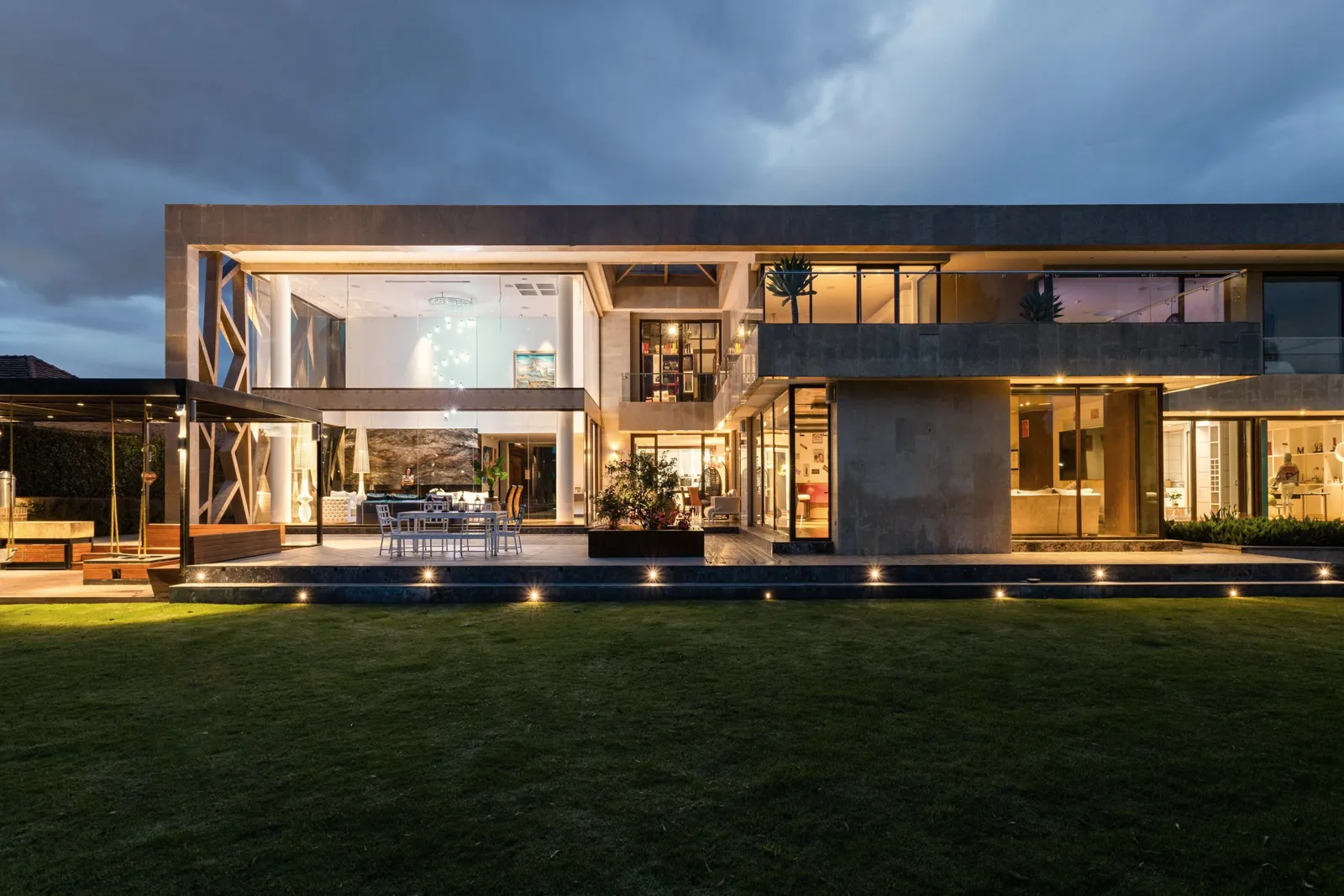 A modern luxury home lit up at dusk, with a lawn in front